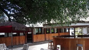 An outdoor seating area with wooden tables and chairs, a Coca-Cola branded umbrella, and a bar counter. - Hotel Hippo Buck (Homa Bay)
