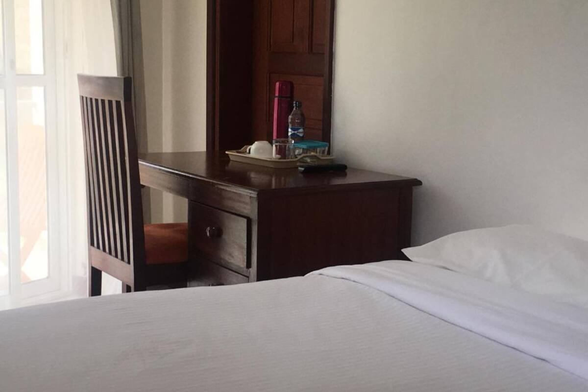 Ein Hotelzimmer mit Bett, Nachttisch aus Holz, Spiegel und einem Fenster mit Vorhängen.