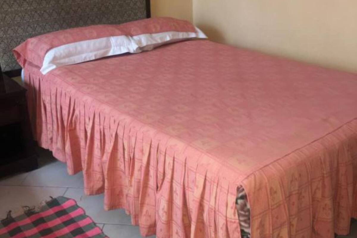 Ein Einzelbett mit pinkener Decke, weißen Kissen, einem karierten Teppich und einem dunklen Kopfteil.