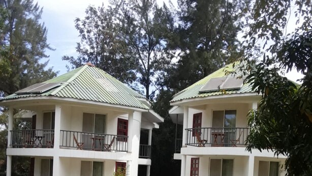 Two white buildings with green roofs and balconies, surrounded by trees and a grassy area. - Hotel Hippo Buck (Homa Bay)
