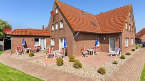 A two-story brick house with a red-tiled roof, a patio with outdoor seating, and a small garden area. - Vacation apartment Seahorse (Esens)