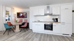 A modern kitchen with white cabinets, a built-in oven, and a dining area with a round table and chairs. - Vacation apartment Seahorse (Esens)