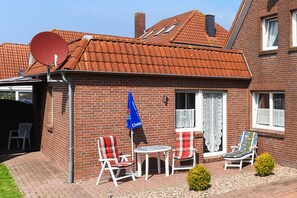 Et murstenshus med tegltag, parabolantenne og en terrasse med havemøbler.