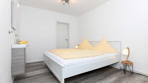 A bedroom with a white bed, a bedside table with a lamp, and a door. - Vacation apartment Seahorse (Esens)