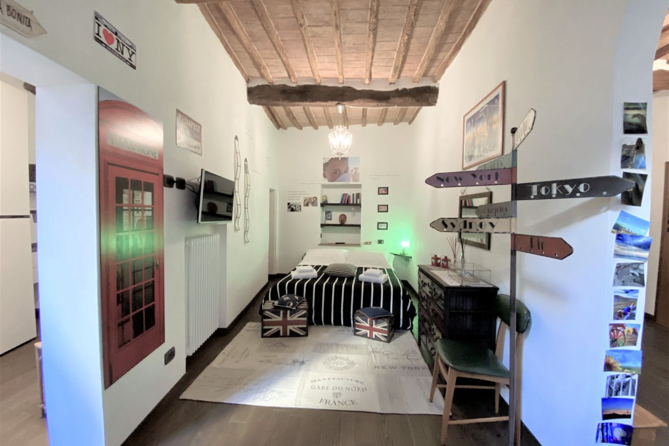 Habitació senzilla amb llit, escriptori i cadira. Hi ha indicadors murals amb direccions cap a diverses ciutats.