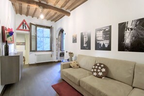 A living room with a sofa, a radiator, a window, and wall-mounted pictures. - IL MONDO DI CLAIRE-cozy and charm (Siena)