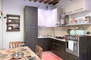 Cozinha compacta com armários escuros, forno de aço inoxidável e mesa de jantar posta com pratos e tigelas.