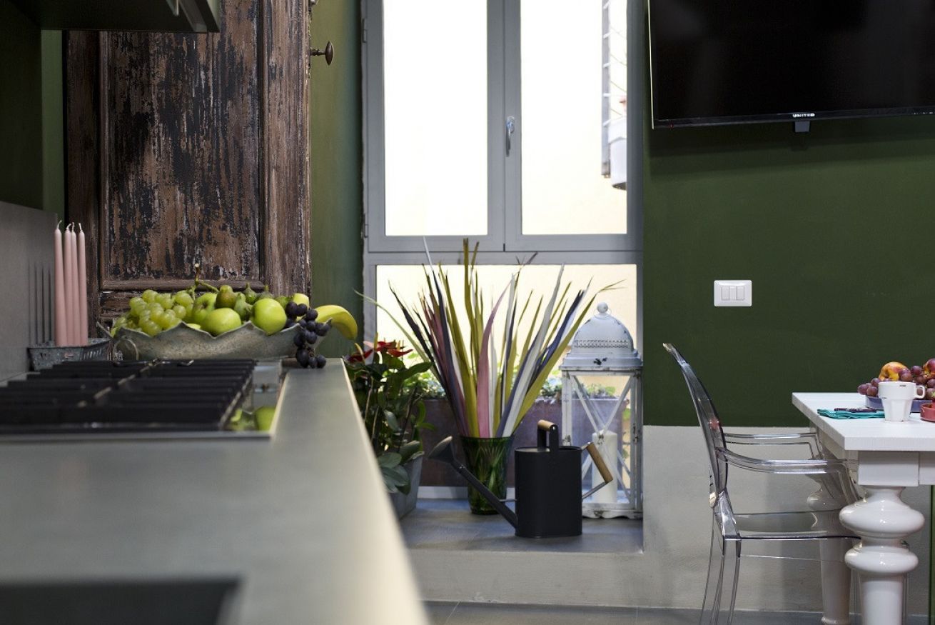 A kitchen area with a wooden cabinet, a window with a view, a table with chairs, and a television mounted on the wall.