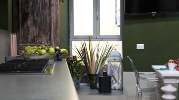 A kitchen area with a wooden cabinet, a window with a view, a table with chairs, and a television mounted on the wall.