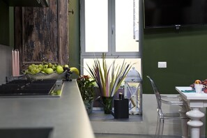 A kitchen area with a wooden cabinet, a window with a view, a table with chairs, and a television mounted on the wall. - LOFT n° 99 - Pavillion Italy (Siena)