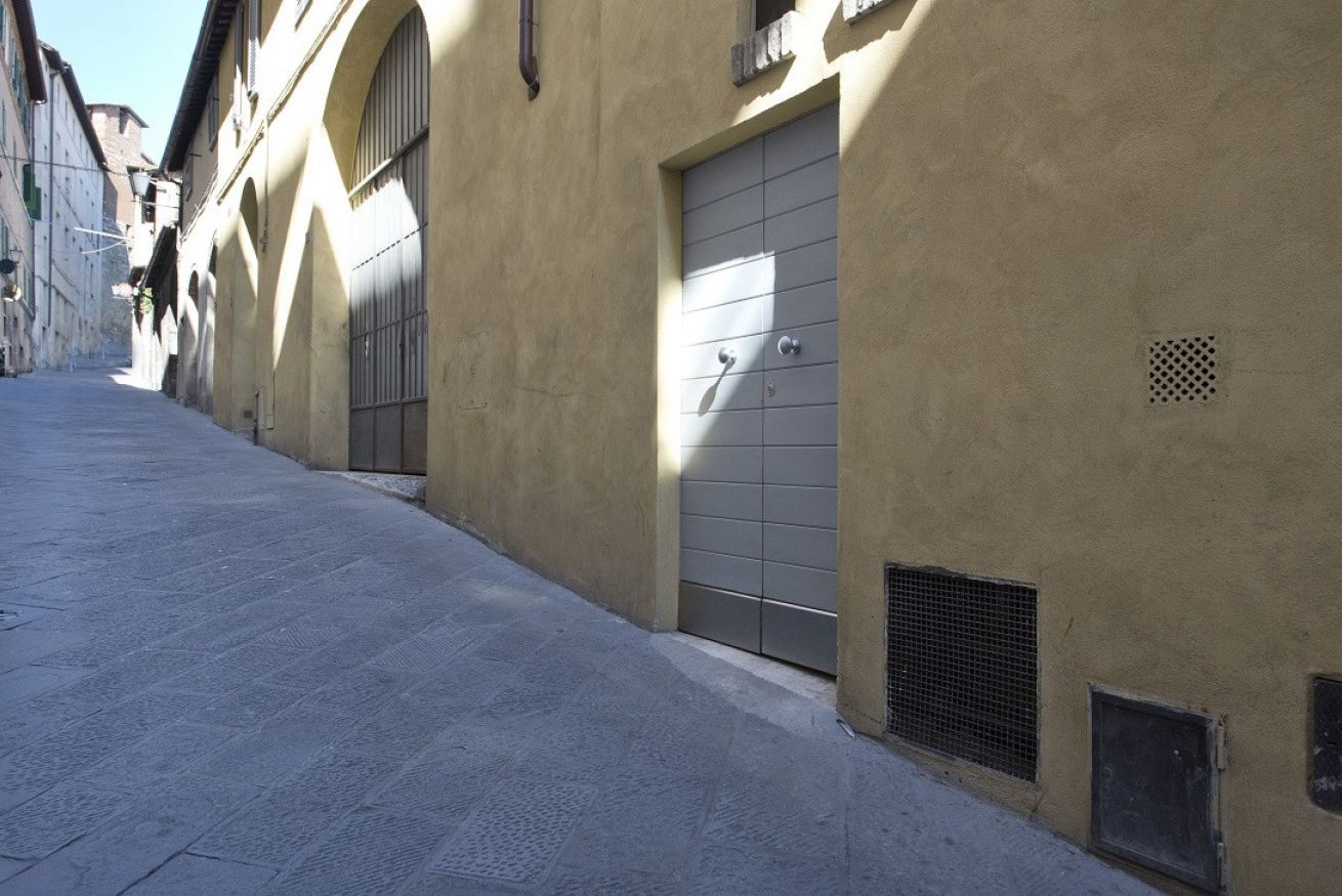 A narrow street with a building featuring a large, closed metal door and a small vent.