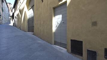 A narrow street with a building featuring a large, closed metal door and a small vent.