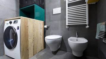 Un baño pequeño con lavadora, inodoro, bidé y un perchero para toallas.