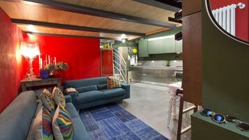 A modern living room with a blue sofa, a red accent wall, and a kitchen area in the background.
