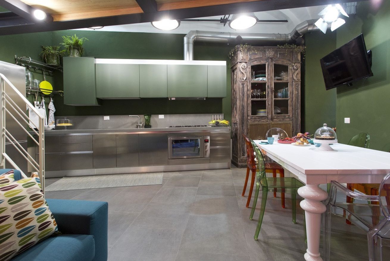 A modern kitchen with stainless steel appliances, a dining area with a white table and colorful chairs, and a green accent wall.