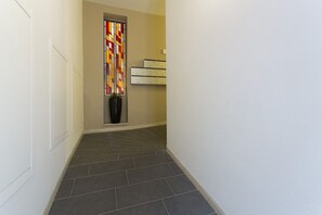 A narrow hallway with dark tiled flooring, a wall-mounted cabinet, and a colorful stained glass window. - LOFT n° 99 - Pavillion Italy (Siena)