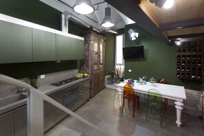 A modern kitchen with green cabinets, a wooden cabinet, a dining table with chairs, and a wine rack. - LOFT n° 99 - Pavillion Italy (Siena)