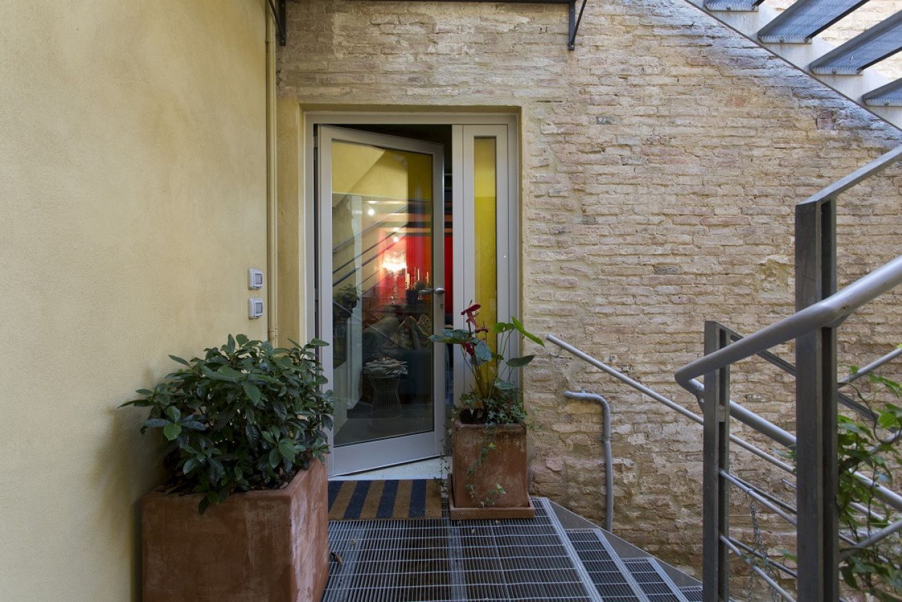 A staircase leading to a door with a glass panel, surrounded by potted plants and a metal handrail.