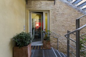 A staircase leading to a door with a glass panel, surrounded by potted plants and a metal handrail. - LOFT n° 99 - Pavillion Italy (Siena)
