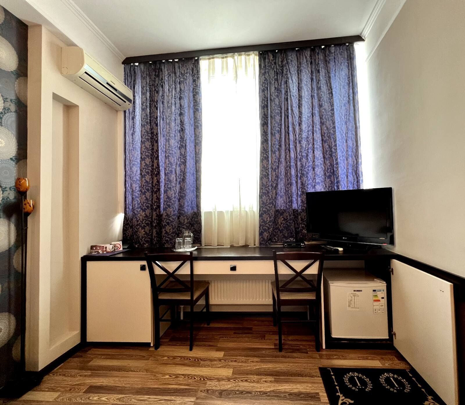 Habitación compacta con escritorio, televisión, refrigerador pequeño y radiador.