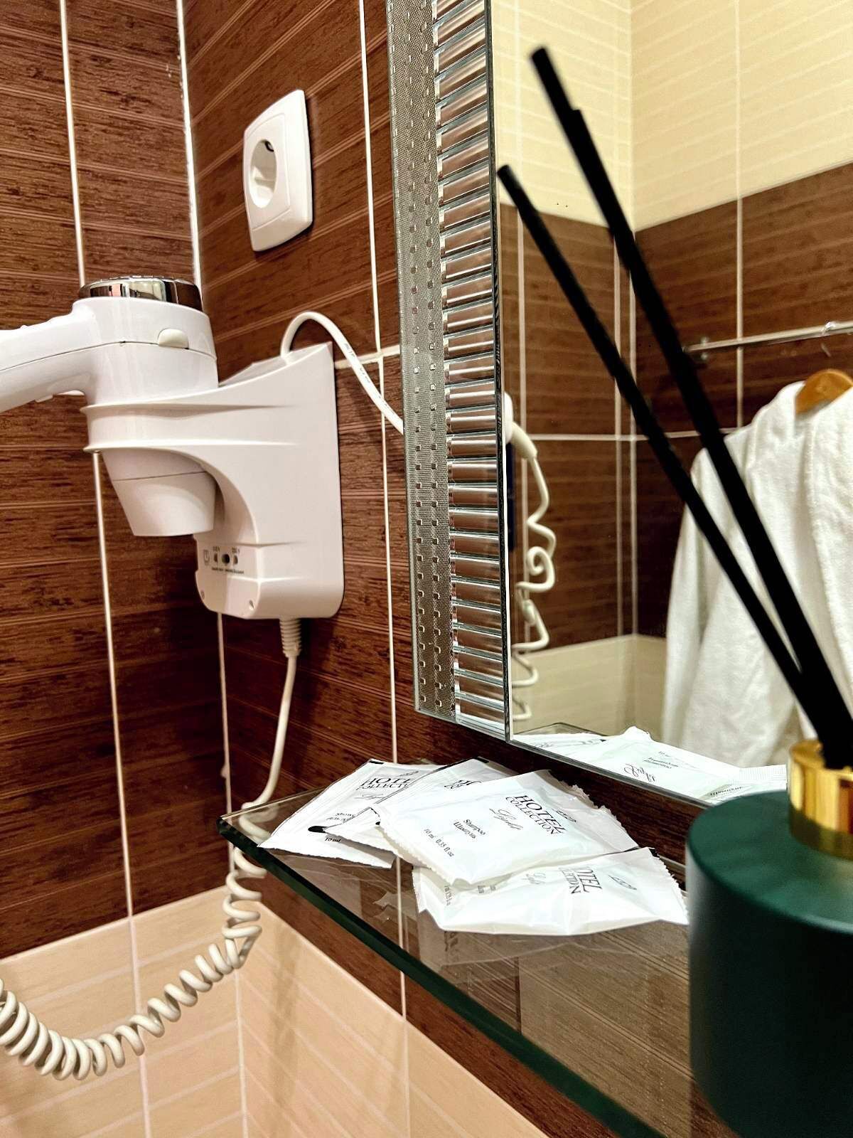 Une salle de bain équipée d’un sèche-cheveux, d’un miroir et d’une étagère en verre où sont rangés les articles de toilette.