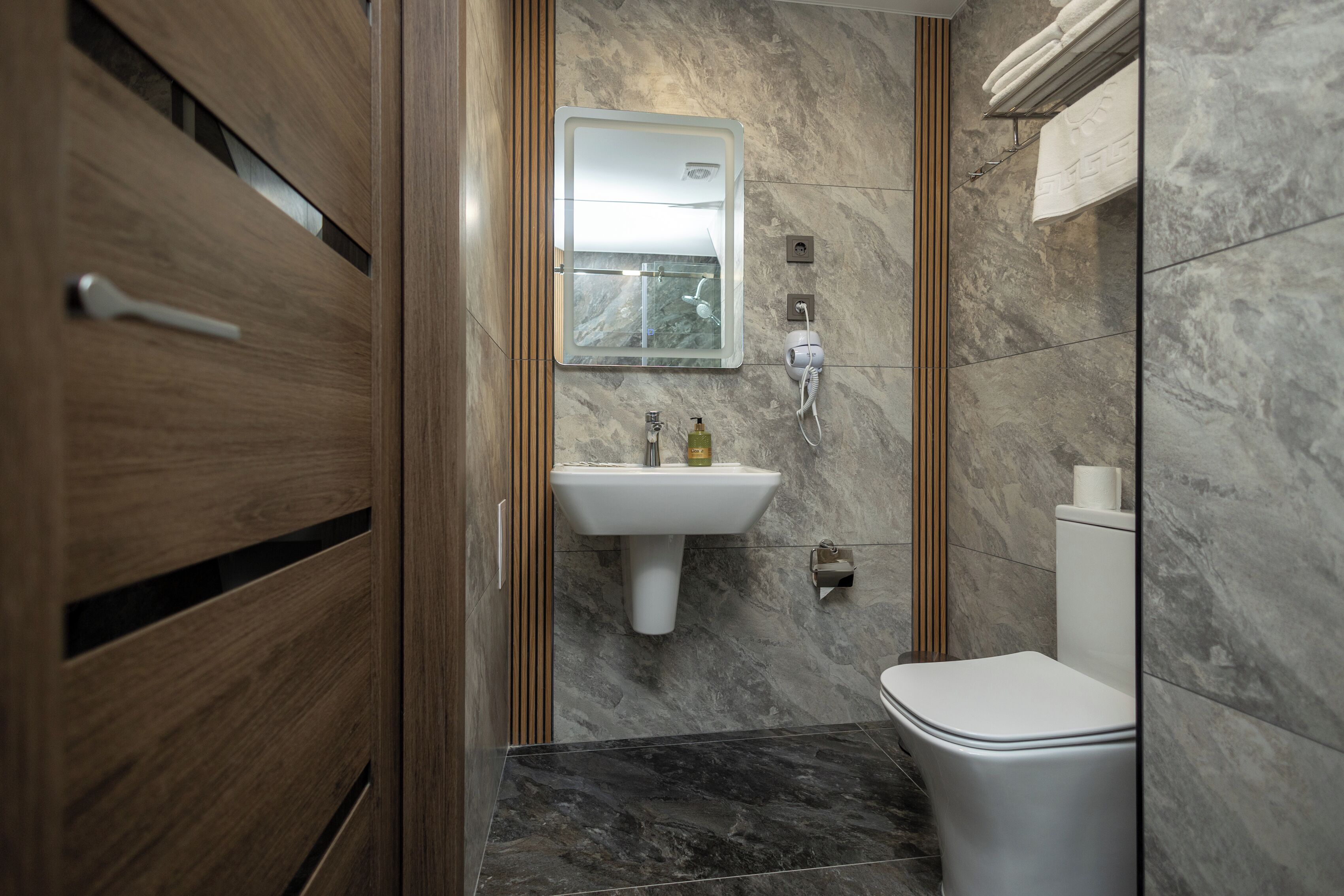 Un baño moderno con tocador de madera, un lavabo blanco, un espejo y un inodoro.