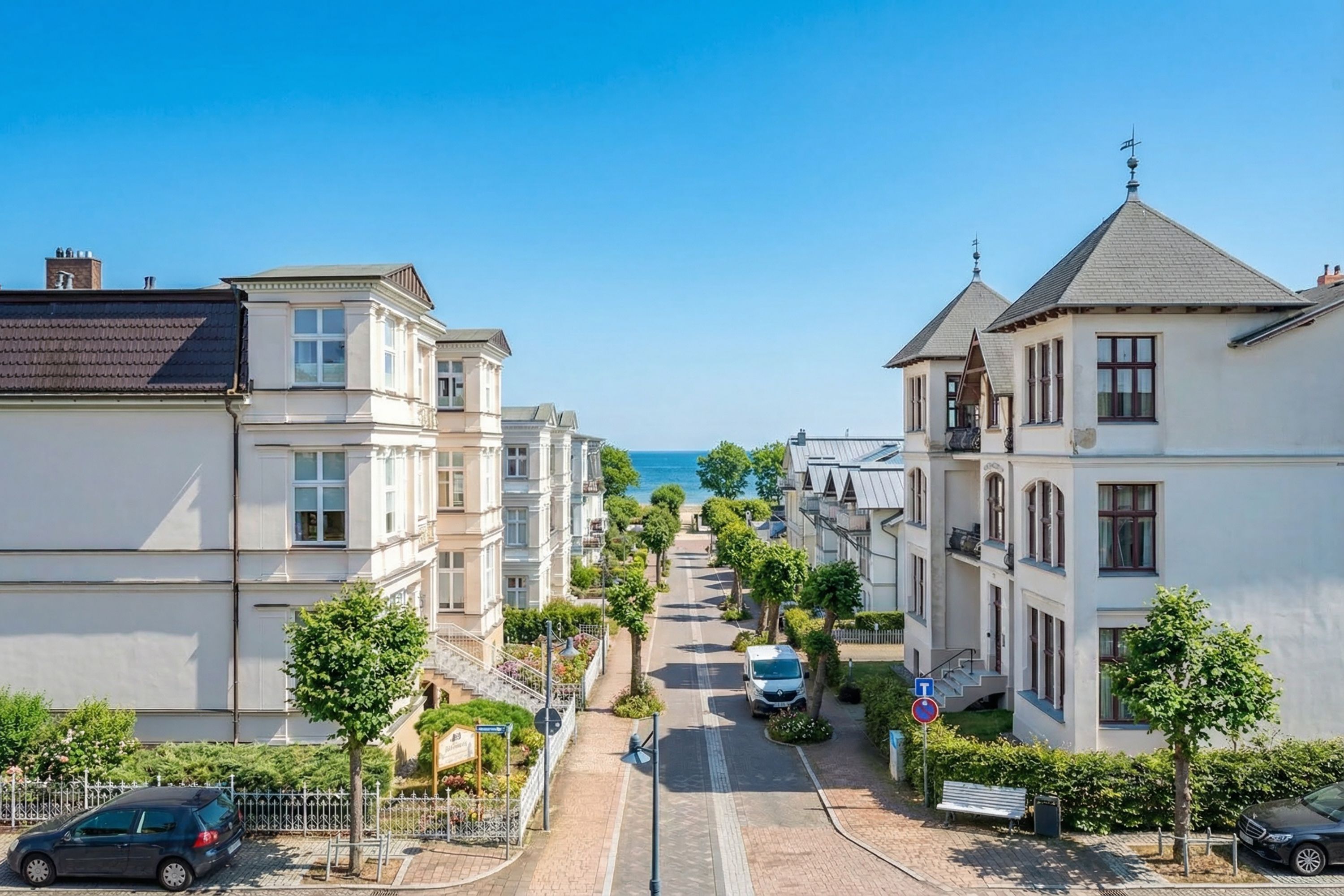 A residential street with houses, a clear sky, and a distant view of the sea.