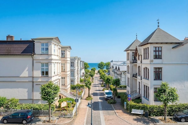A residential street with houses, a clear sky, and a distant view of the sea.