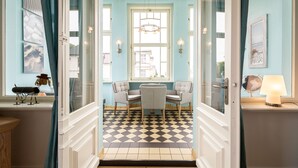 Une pièce avec un sol à carreaux, deux chaises, une table, une fenêtre avec des rideaux, des appliques murales et une lampe.