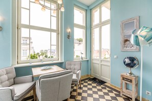 Une pièce avec un sol à carreaux, une table entourée de chaises, de grandes fenêtres et un globe terrestre posé sur une petite table.