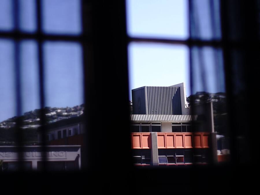 Ein Fenster mit Rasteroptik, durch das ein Gebäude mit modernem Design und Flachdach sichtbar ist.