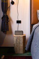A small bedside table with a speaker, a robe hanging on the wall, and a bed with a quilt.