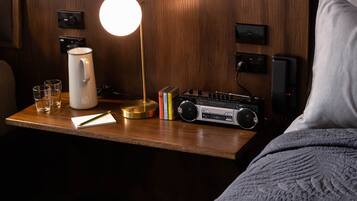 A wooden nightstand with a radio, books, glasses, a notepad, and a lamp.