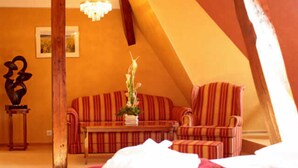 A cozy, triangular room with a striped sofa, a small table, and a decorative plant. - Junior suite castle lakeside - Seehotel Schloss Klink (Klink)