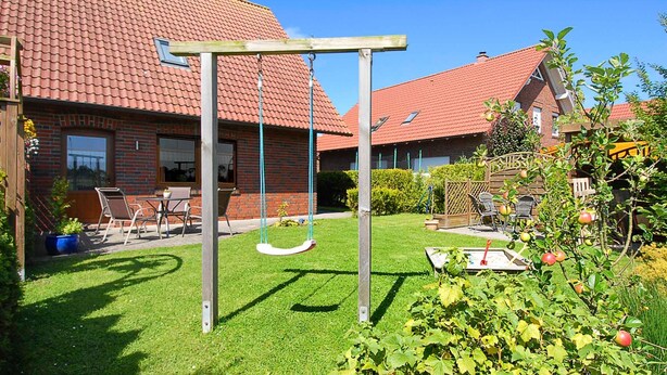 Un patio trasero residencial con un tobogán, una casa de ladrillo y un jardín con manzanos.