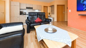 Una sala de estar moderna con un sofá de cuero negro, una mesa de centro de madera y una cocina al fondo.