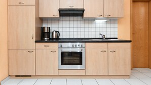 Una cocina con armarios de madera clara, horno de acero inoxidable, cafetera y salpicadero de azulejos.