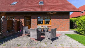 Una casa de ladrillo con techo de tejas rojas, un patio con muebles de mimbre y un ventanal pequeño.