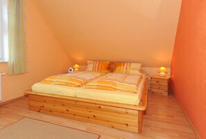 A bedroom with a wooden bed, two bedside tables with lamps, and a window with curtains. - Vacation apartment Flut - Holiday apartments Haus Meeresleuchten (Esens)