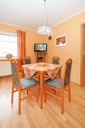 A dining area with a wooden table, four chairs, a television, and a clock on the wall. - Vacation apartment Flut - Holiday apartments Haus Meeresleuchten (Esens)