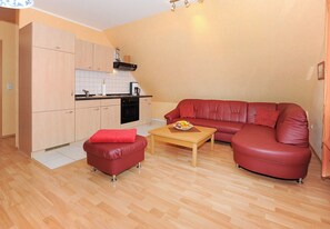 A compact living space with a kitchenette, a red leather sofa, a matching ottoman, and a wooden coffee table. - Vacation apartment Flut - Holiday apartments Haus Meeresleuchten (Esens)