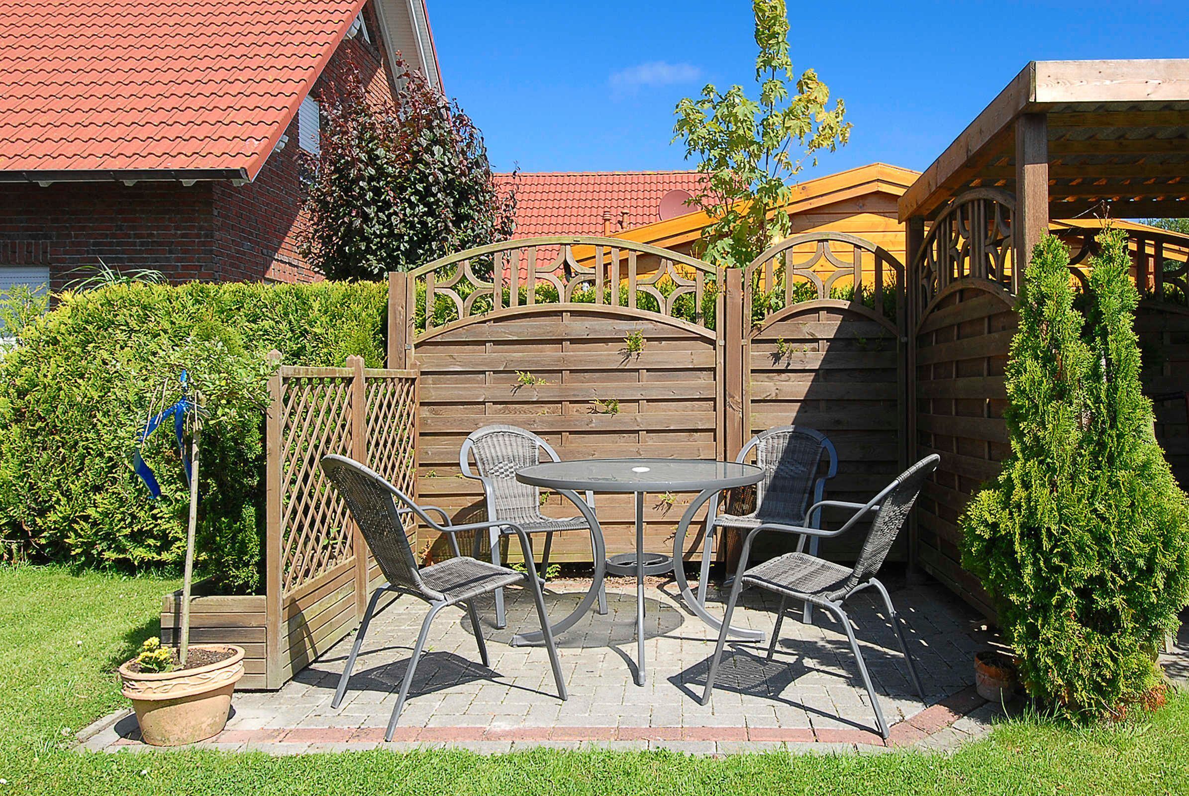 A patio with a table and four chairs, surrounded by a wooden fence and greenery.