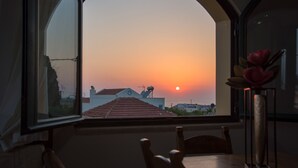 A view through an arched window of a sunset over a cityscape, with a table and chairs in the foreground. - Skandalis Apartments with sea & pool view (Klio) (CHORAFAKIA CHANIA)
