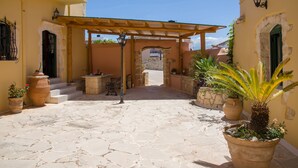A courtyard with a wooden pergola, stone flooring, and potted plants. - Skandalis Apartments with sea & pool view (Klio) (CHORAFAKIA CHANIA)