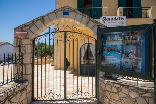Une porte en pierre traditionnelle, surmontée d’une enseigne indiquant « Skandalis », signale la présence d’une suite de style traditionnel à louer.