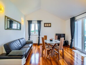 Una sala de estar moderna con un sofá de cuero negro, una mesa de comedor de madera y sillas. Hay un ventanal con cortinas, un televisor de pantalla plana y un cuadro en la pared.