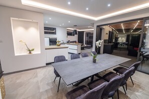 A modern kitchen with a central island, a dining area with a large table and chairs, and a living area with a sofa and coffee table.