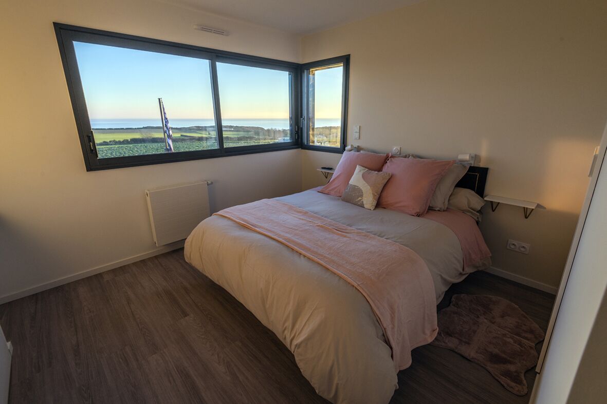 A bedroom with a large window, a bed with pink bedding, and a radiator.