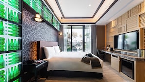 Une chambre d’hôtel moderne avec un grand lit, une télévision, un minibar et un mur décoré de bouteilles vertes.