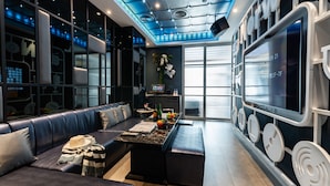 Un hall d’hôtel moderne avec un canapé en cuir, un petit coin bar et un grand écran numérique.